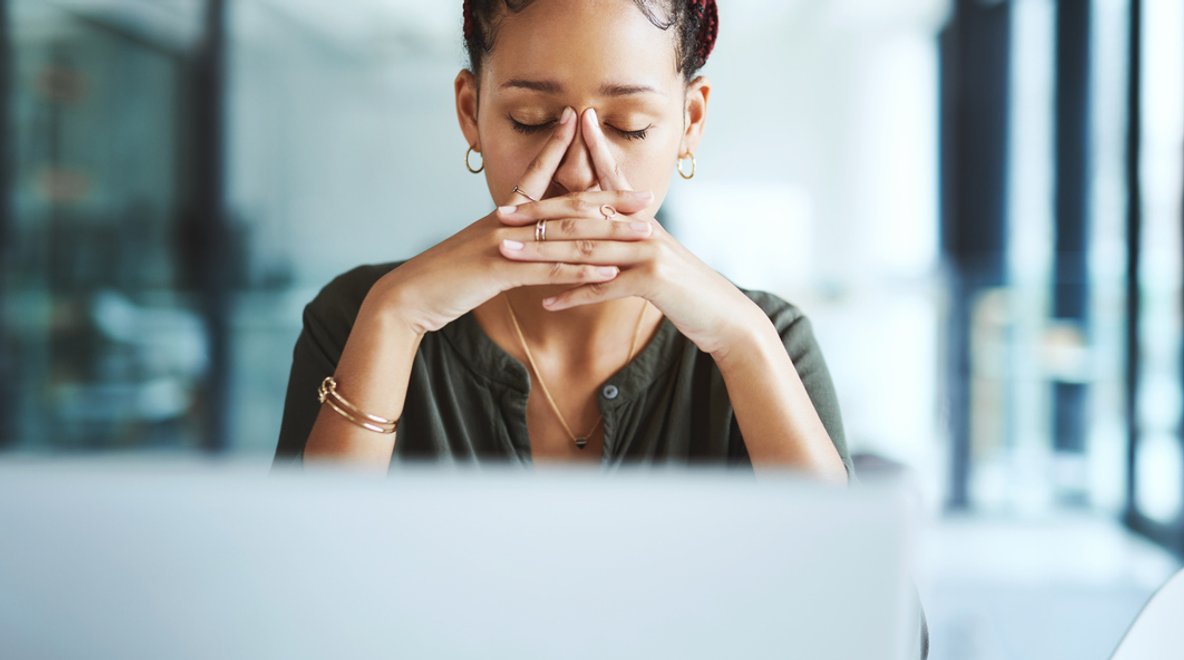 Person sitting at a desk with a laptop, hands clasped near face