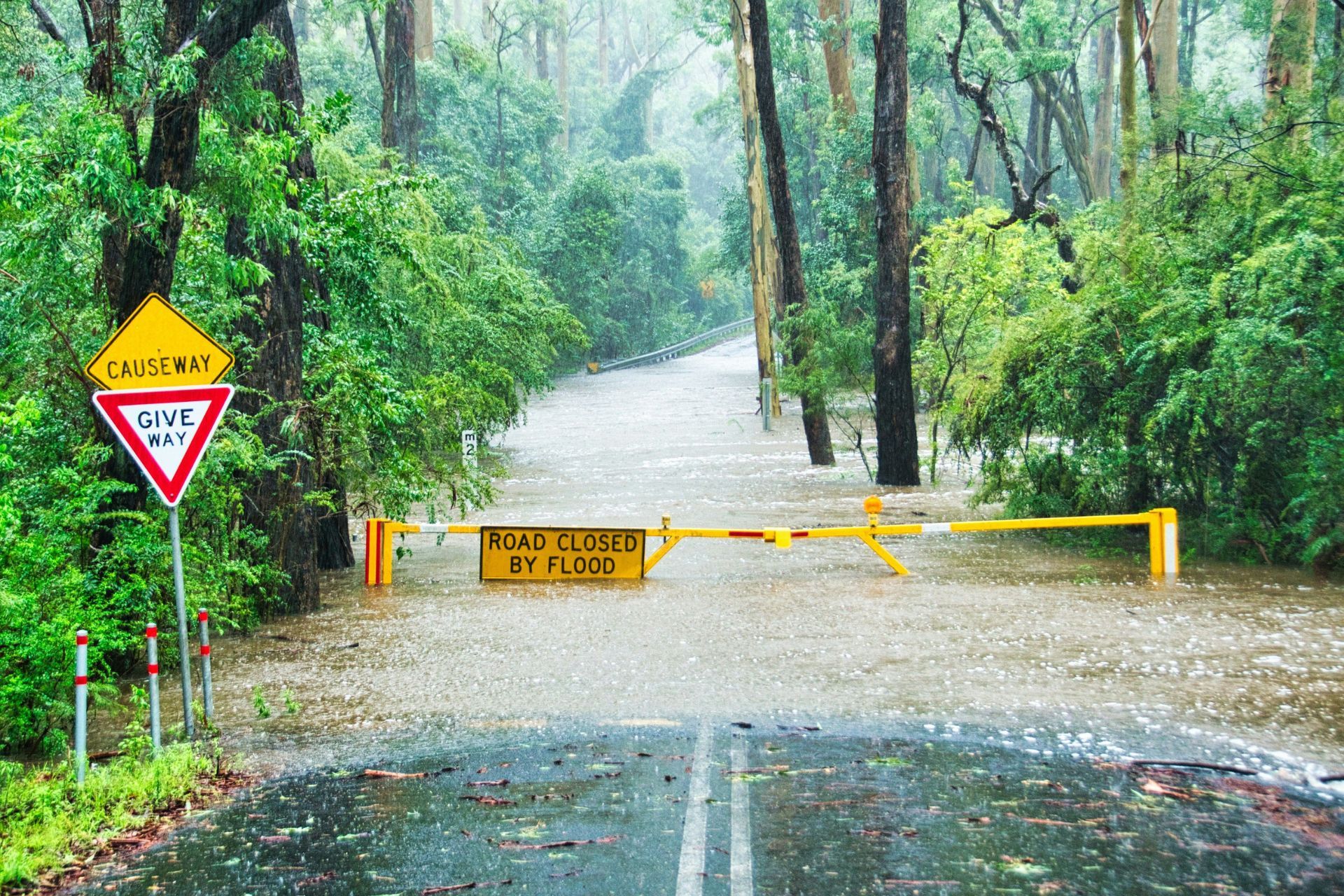 Floodwater covering a remote road with a road closure barrier and warning signs.