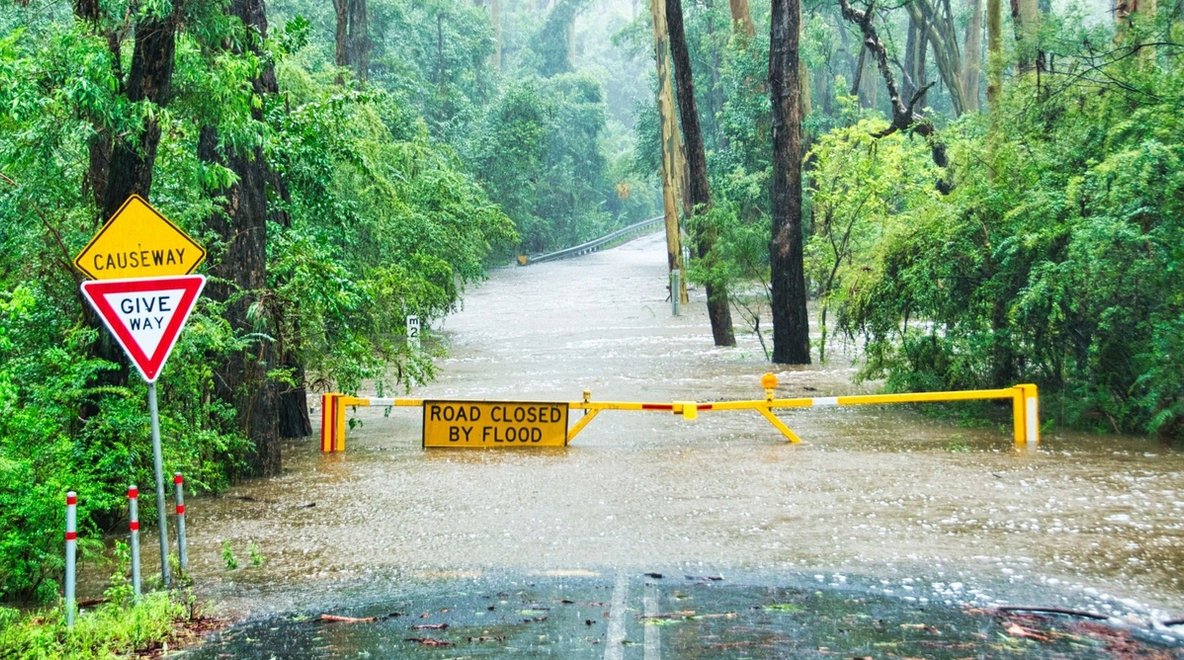 Floodwater covering a remote road with a road closure barrier and warning signs.