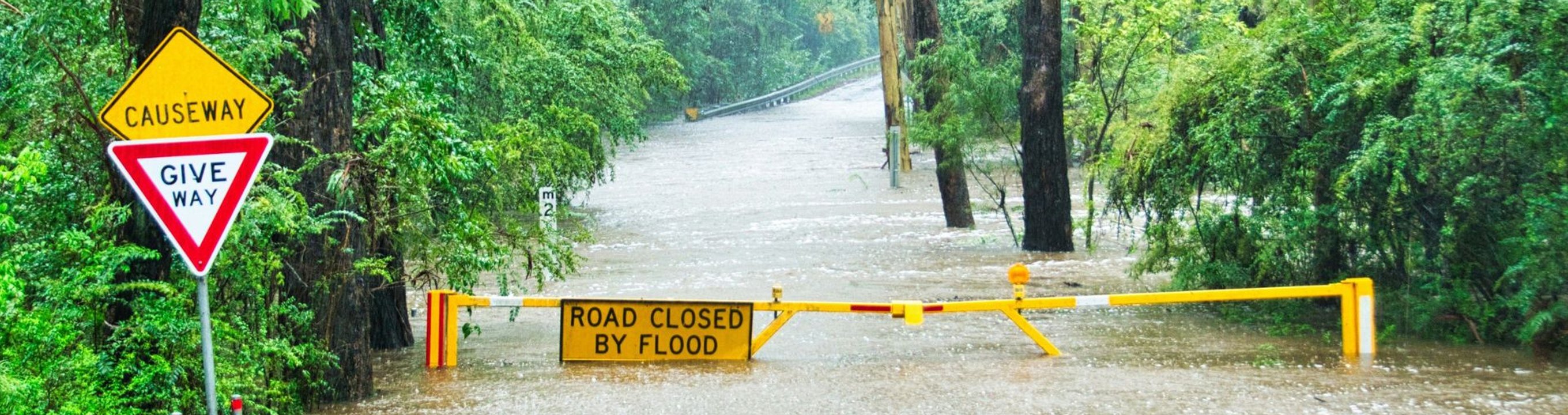 Floodwater covering a remote road with a road closure barrier and warning signs.
