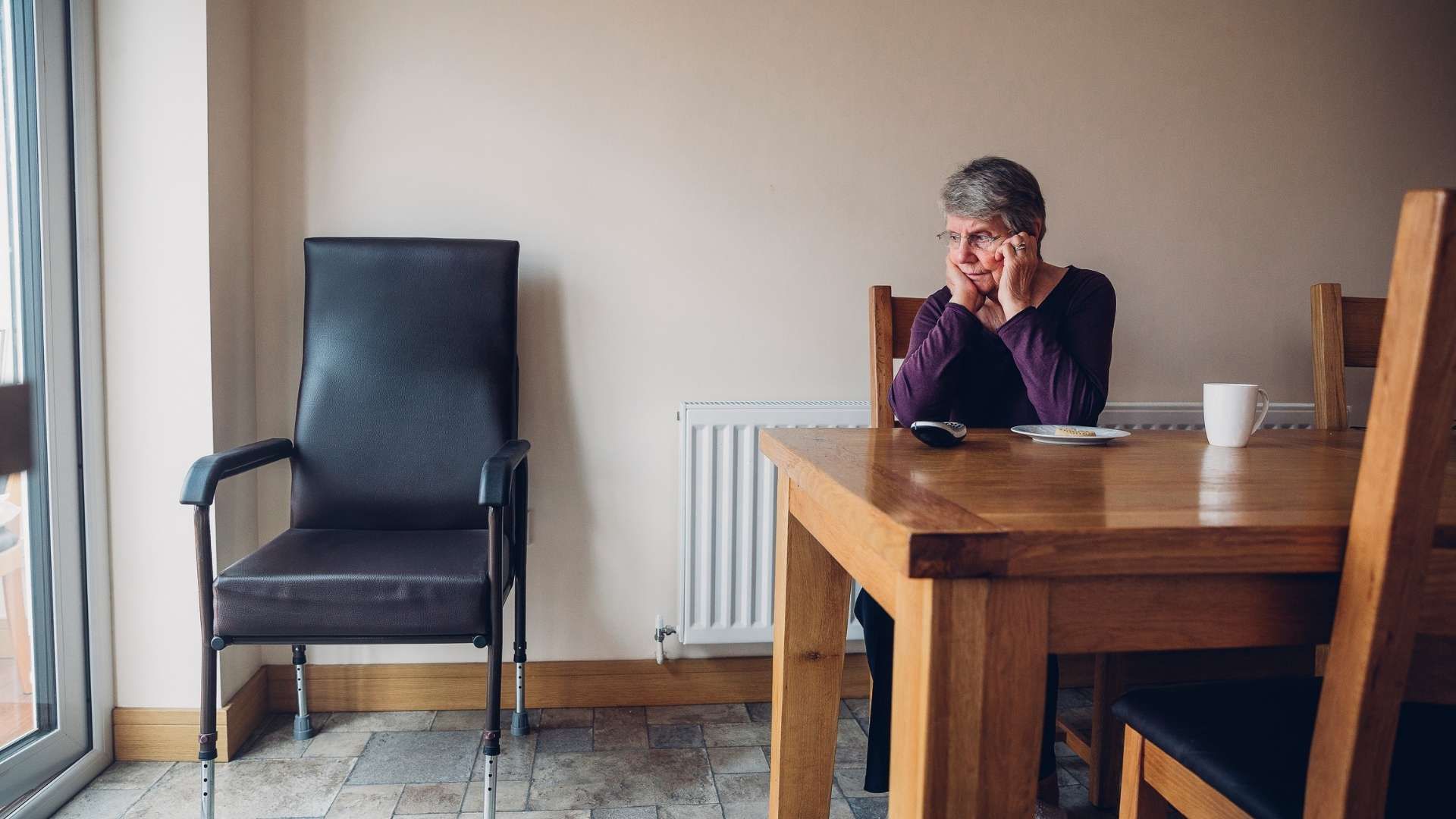 Older person sitting at a table alone with a phone nearby