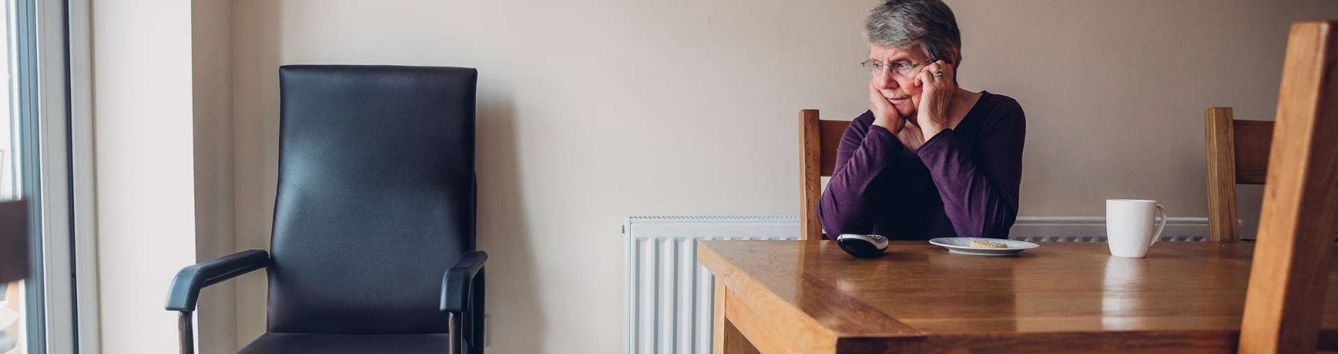 Older person sitting at a table alone with a phone nearby