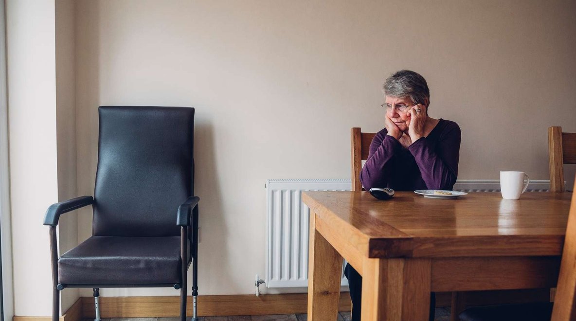 Older person sitting at a table alone with a phone nearby