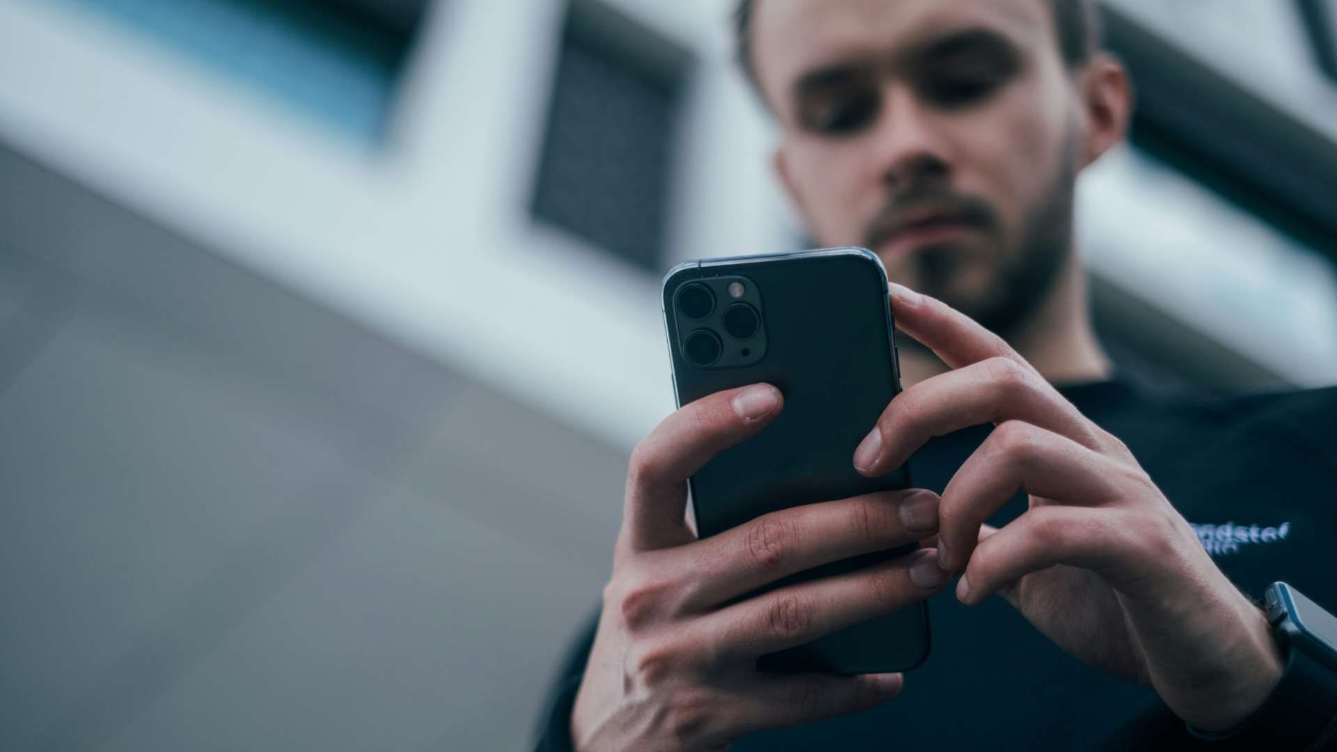 Person using a smartphone outdoors with a blurred building in the background