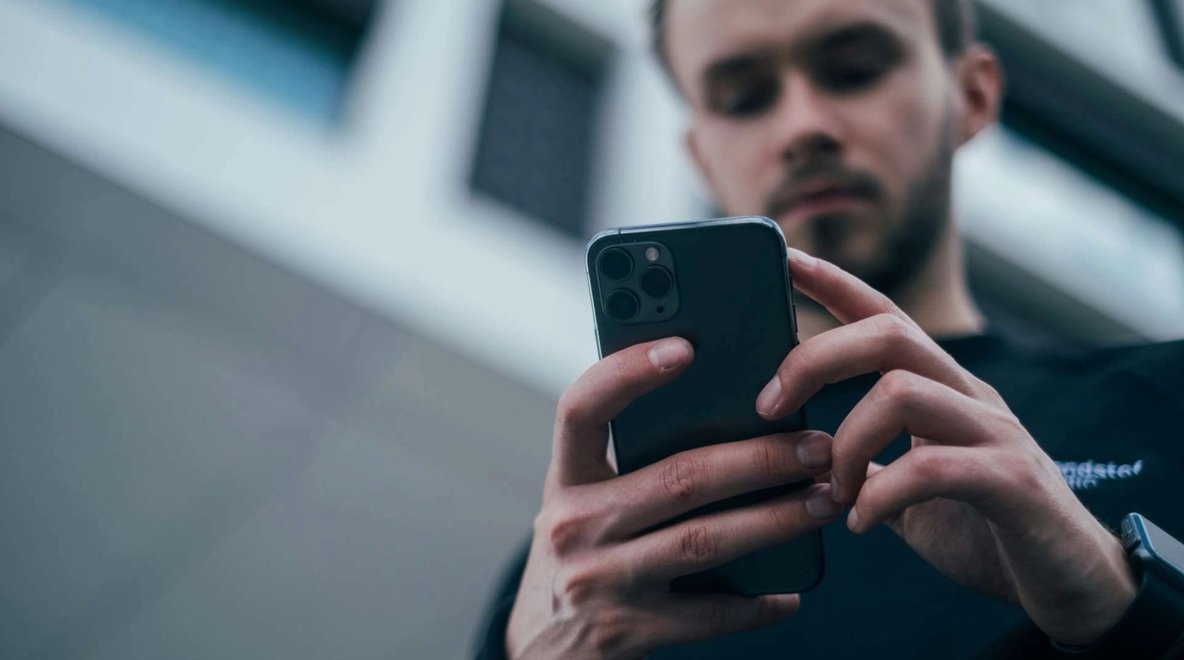 Person using a smartphone outdoors with a blurred building in the background