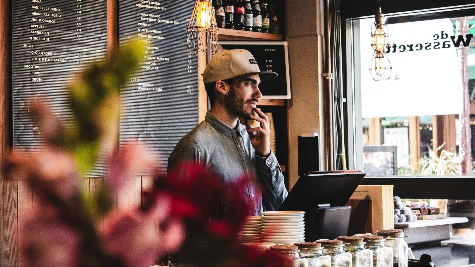 Person standing behind café counter with menu board and window in background