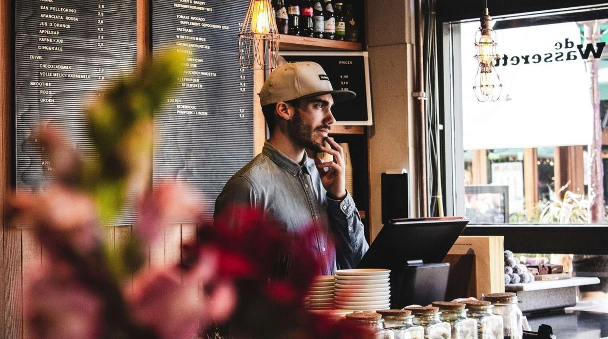 Person standing behind café counter with menu board and window in background
