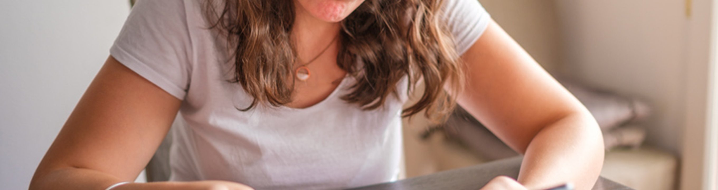Person sitting at a table, checking a smartphone while writing notes in a notebook.